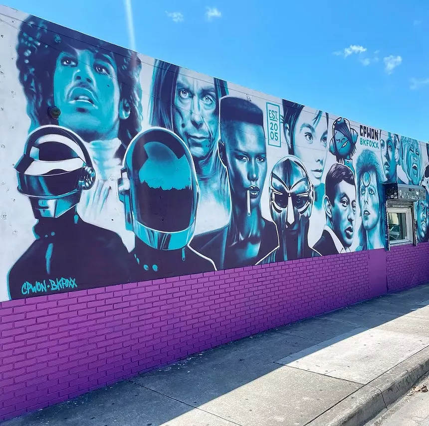 a purple and teal mural depicts music legends Prince, Daft Punk, Iggy Pop, Grace Jones, Bjork, David Bowie, and others