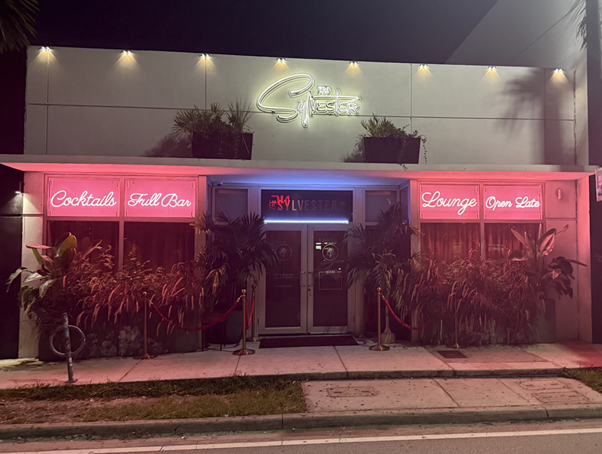 The front of a building with a pink neon sign