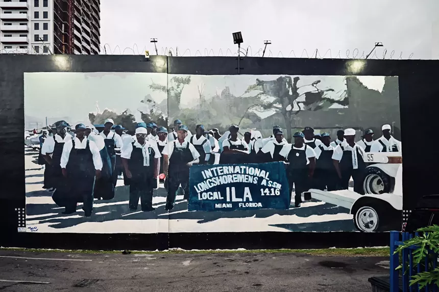 a mural on a black wall depicts a group of men in overall uniforms and hard hats posing in front of a banner reading, "International Longshormens Assn, Local ILA 1416, Miami Florida"