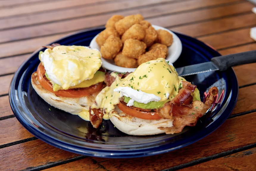 eggs Benedicts on a blue plate with side of tater tots