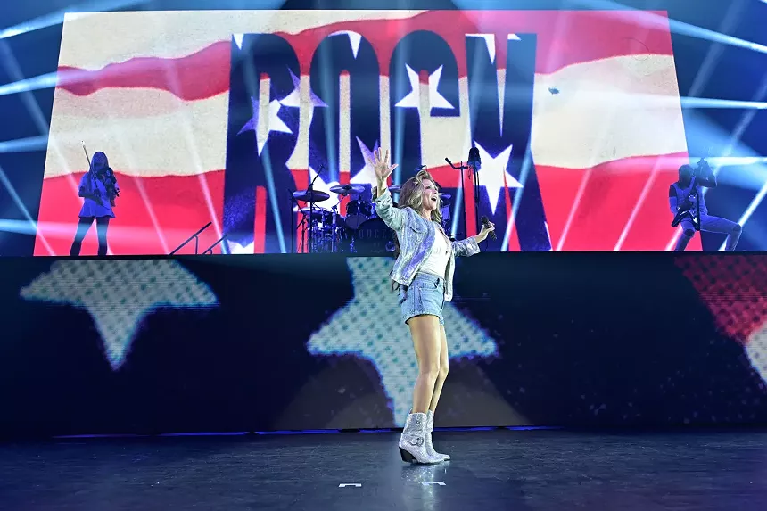 A woman on stage in front of an LED screen with the American flag.