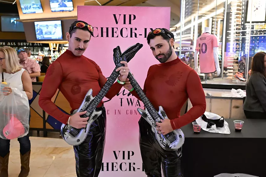 Two people wearing red mesh shirts and holding inflatable guitars.