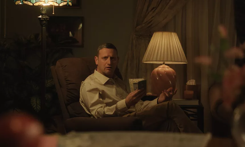 a man sitting on a recliner in a dimly lit room looks perplexed