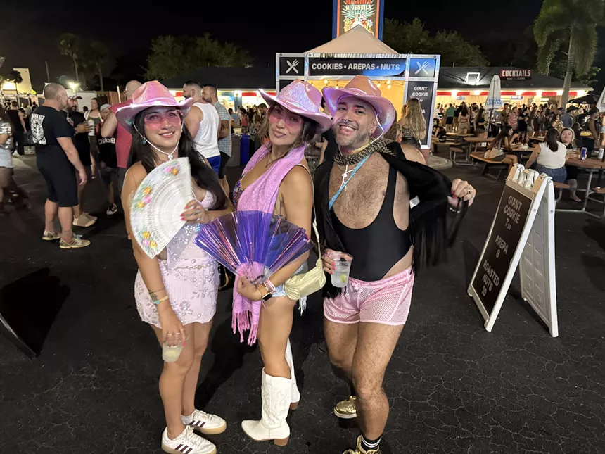 Three people wearing pink cowboy hats outside a concert in South Florida.