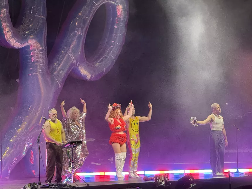 A concert stage with performers and an inflatable pair of giant scissors