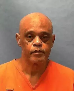A photo of an older bald Black man wearing an orange  prison jumpsuit.