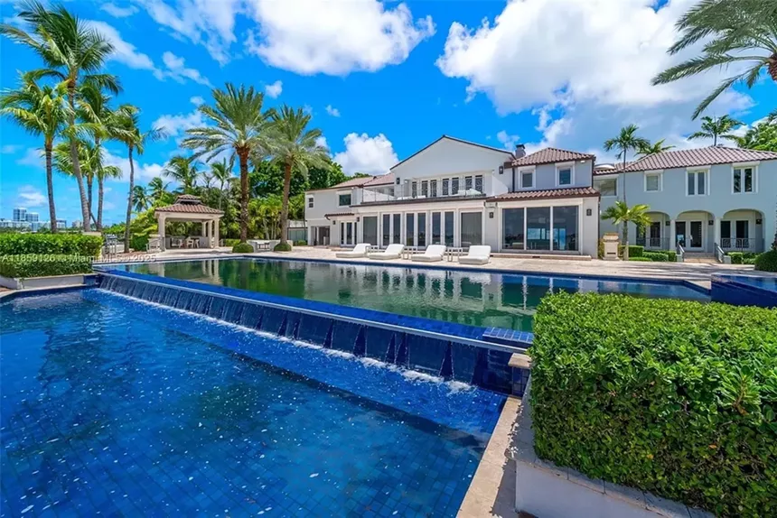 Pictured is a backyard poolside oasis, surrounded by lounge chairs and thick South Florida shrubs and trees.