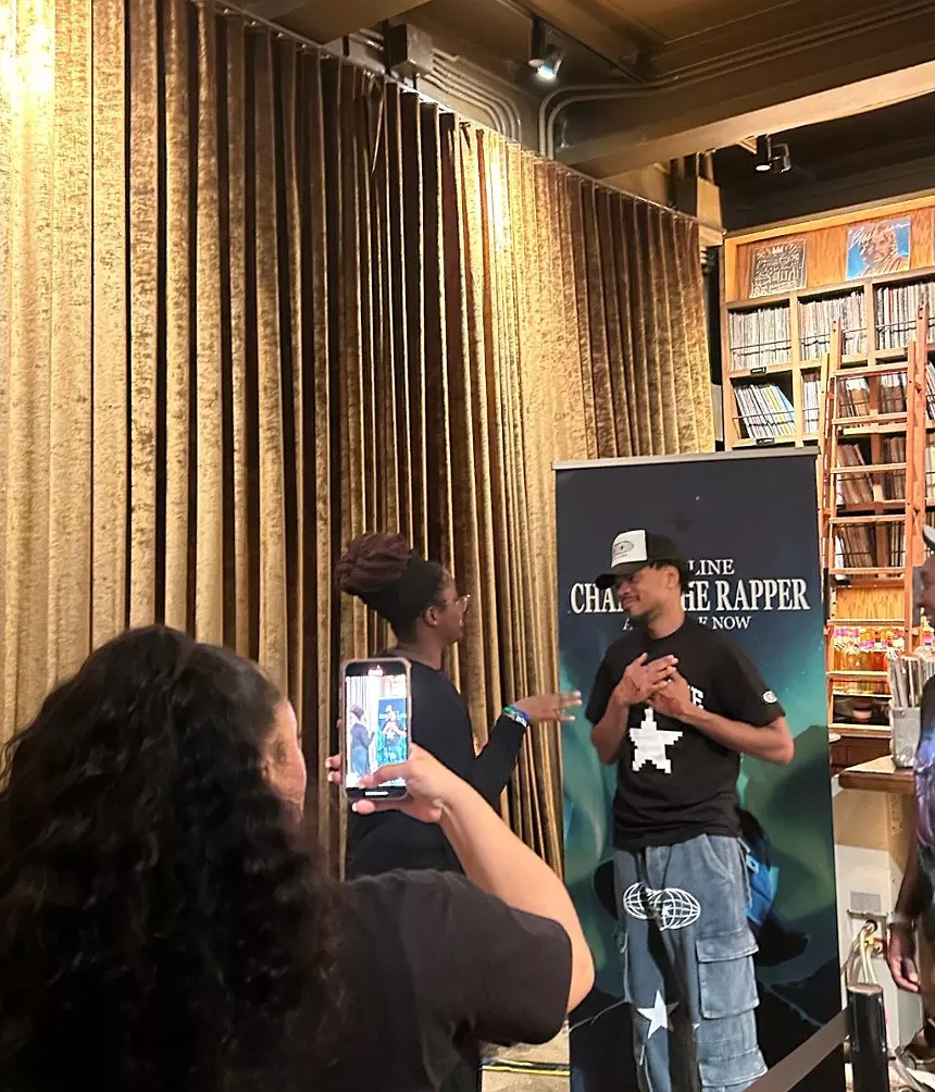 Image of two people at a meet and greet standing by a promotional banner.
