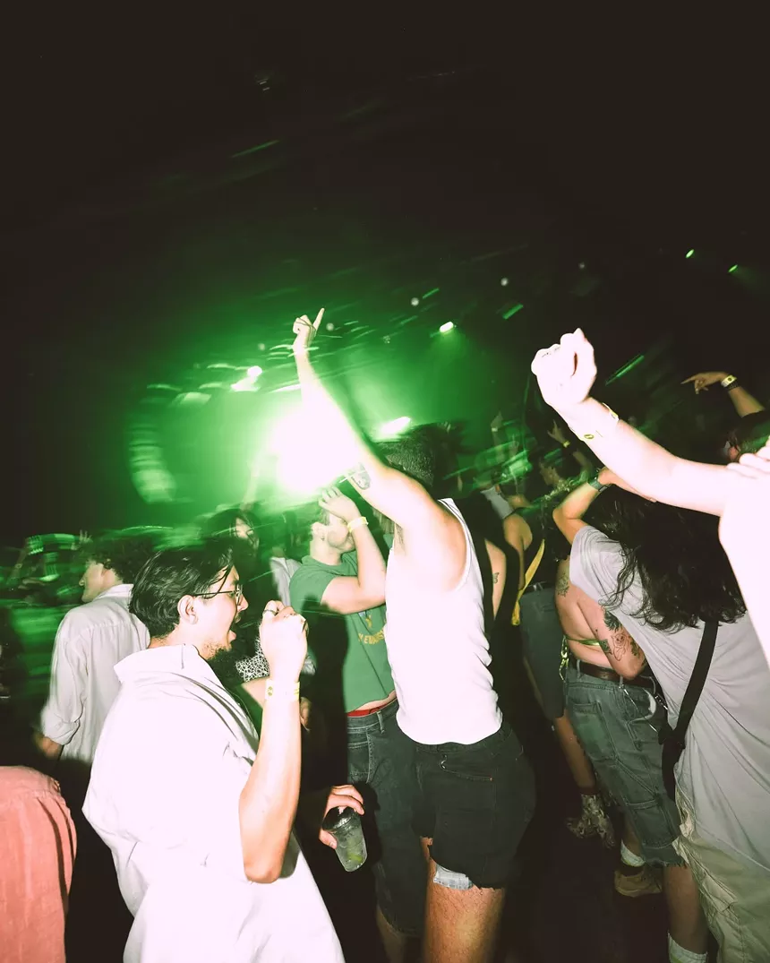 Young people dancing at a club under green lights.