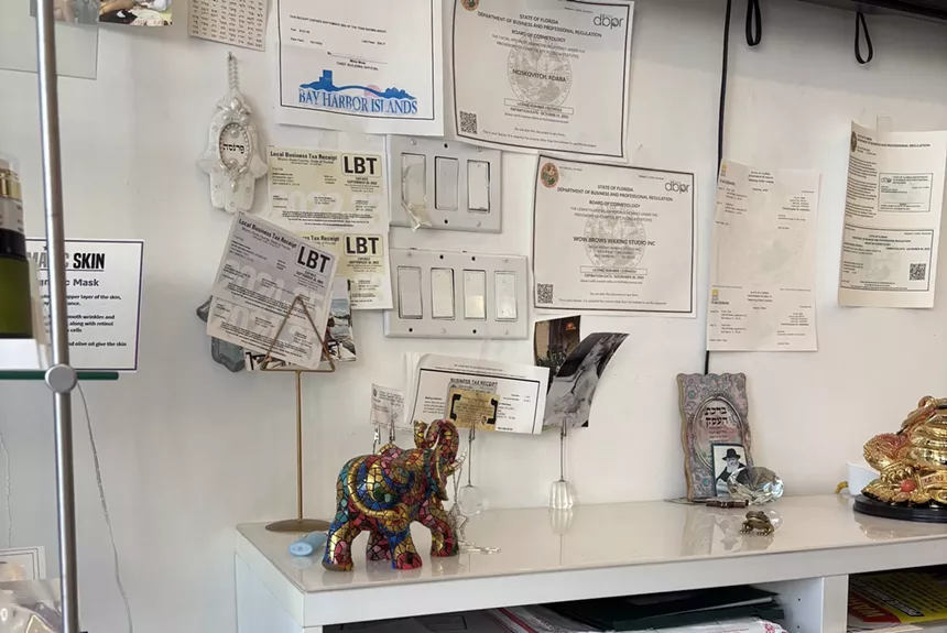 A white shelf with an elephant figurine on it, plus Florida department of cosmetology permits posted on the wall