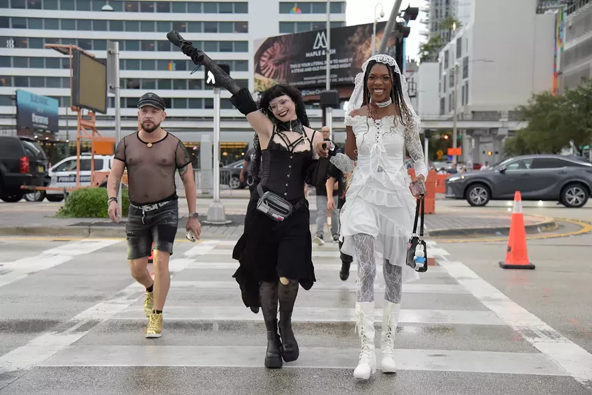 three Lady Gaga fans on a crosswalk wearing a mesh and leather outfit, a black lacey corseted outfit, and a white lacey corseted outfit