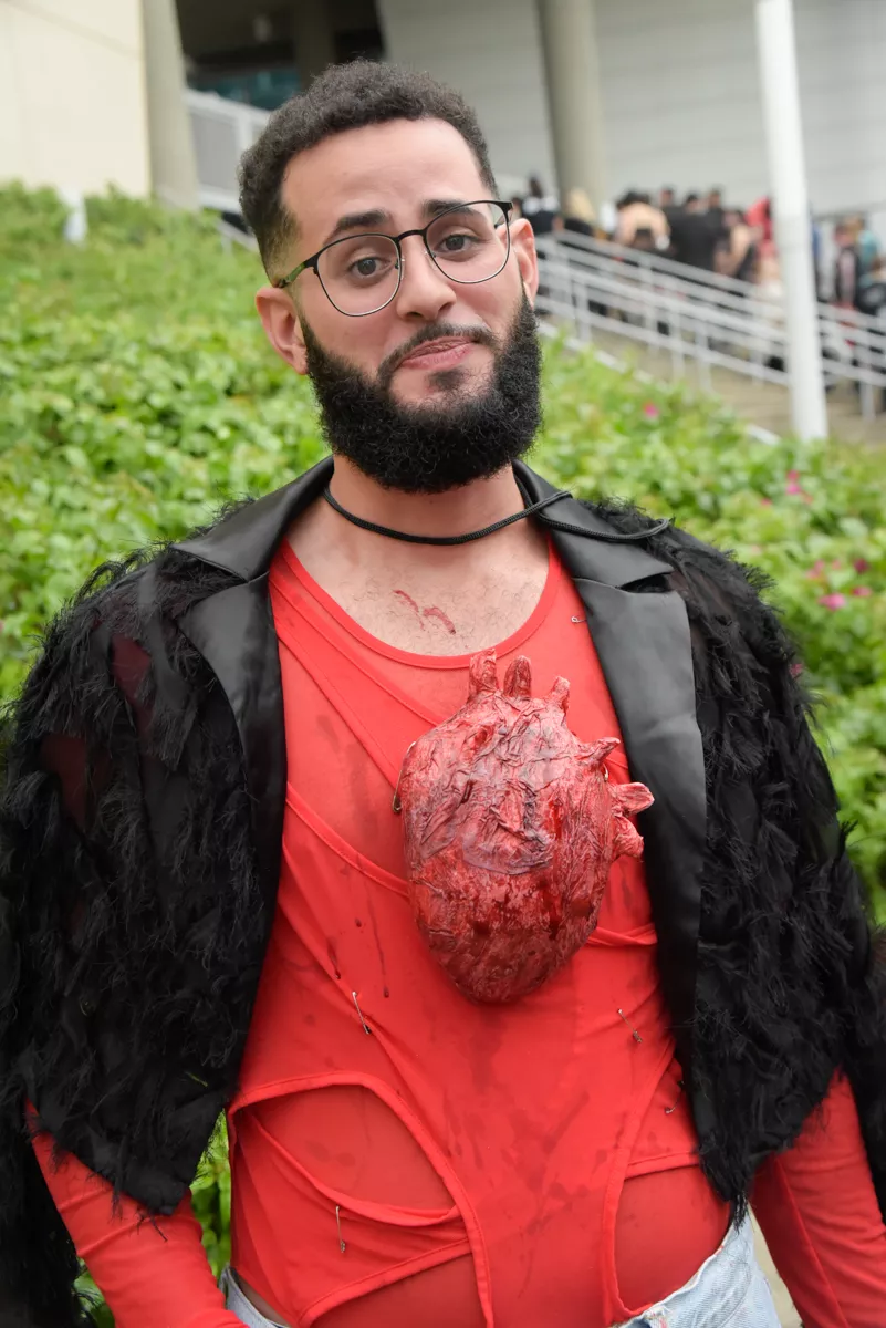 a person wears a red DIY bodysuit with a black textured blazer and an effigy of a human heart on their chest
