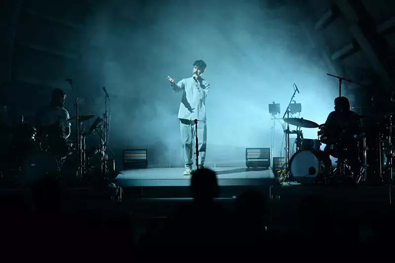 Image: a band performing on an amphitheater stage under eerie, cloudy lighting