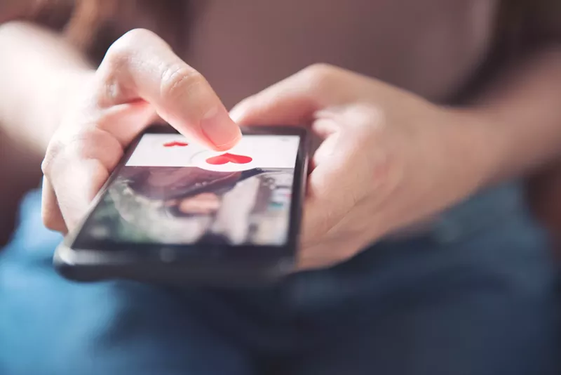 Image: Hands on a phone with a dating app on the screen