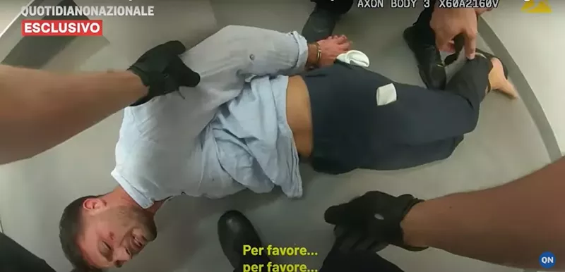 Image: A student is lying face down on the floor of a holding cell, with his handcuffed hands behind his back