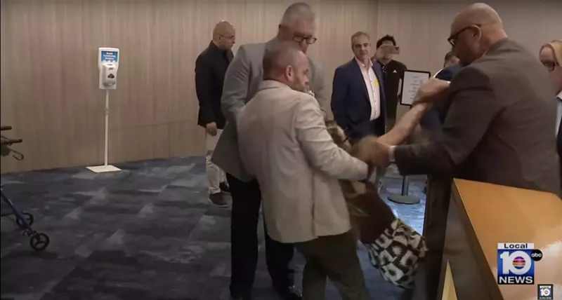 Image: A photo of Miami-Dade Sheriff's Office deputies in khaki and gray suits forcibly removing a woman who was reportedly protesting an Immigration and Customs Enforcement (ICE) agreement with county jails.
