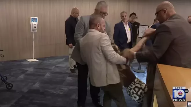 A photo of Miami-Dade Sheriff's Office deputies in khaki and gray suits forcibly removing a woman who was reportedly protesting an Immigration and Customs Enforcement (ICE) agreement with county jails.