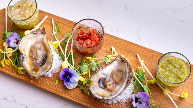 A platter of oysters and herbs on a wooden cutting board.