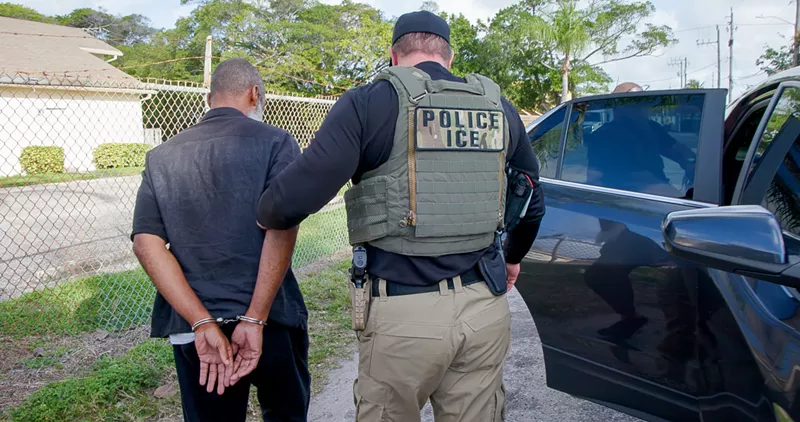 Image: An ICE agent holds a man in handcuffs