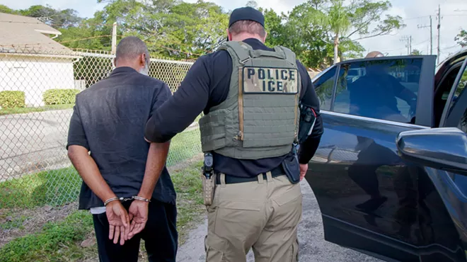 An ICE agent holds a man in handcuffs