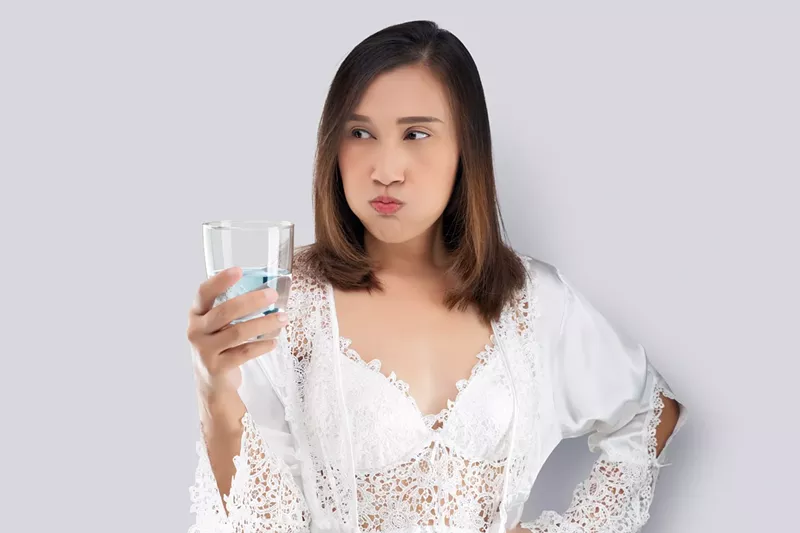 Image: Woman in white silk nightwear and lace robe rinsing with mouthwash against a gray background