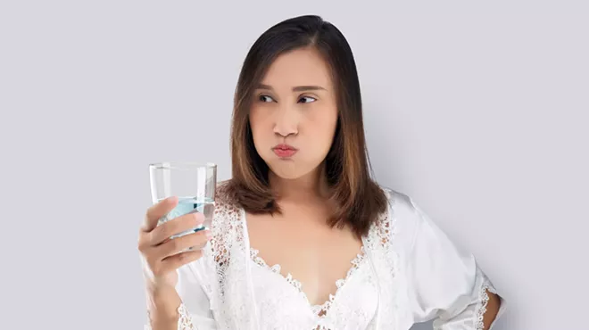 Woman in white silk nightwear and lace robe rinsing with mouthwash against a gray background