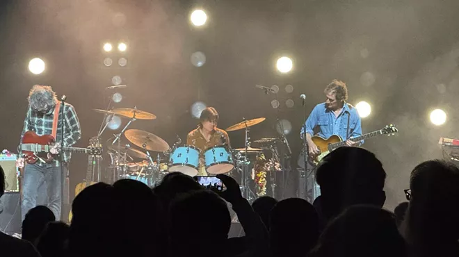 A rock band on stage, rocking, with the silhouettes of audience members in the foreground