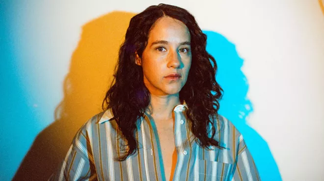 photo of a woman in a striped button down shirt against a vaguely psychedelic background