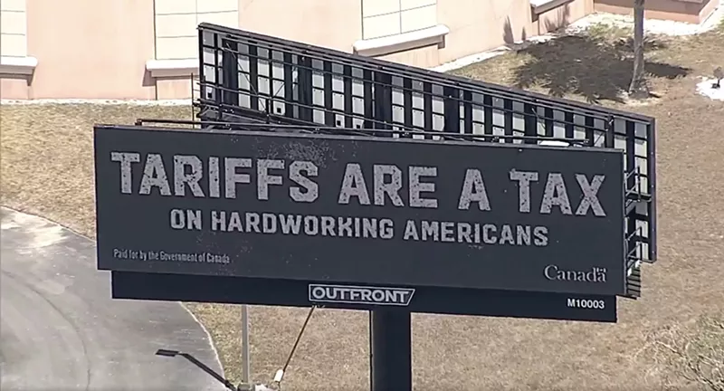 Image: screenshot of an aerial shot of a billboard that reads: "TARIFFS ARE A TAX ON HARDWORKING AMERICANS."