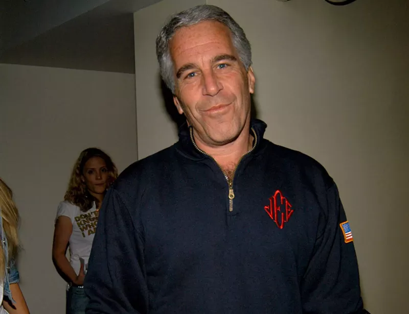 Image: Jeffrey Epstein looking at the camera wearing the blue quarter zip sweatshirt with red monogrammed initials