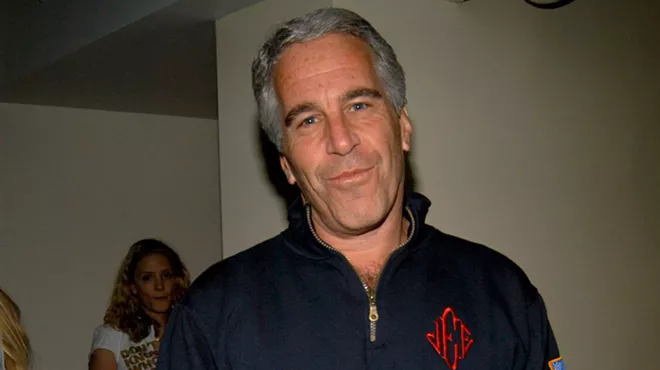 Jeffrey Epstein looking at the camera wearing the blue quarter zip sweatshirt with red monogrammed initials