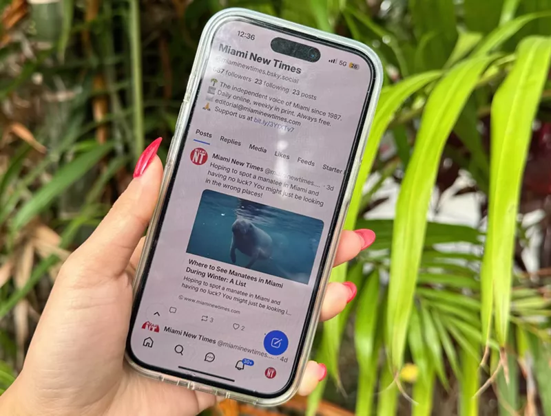Image: photo of a woman's hand holding a smartphone with the Miami New Times profile on Bluesky.