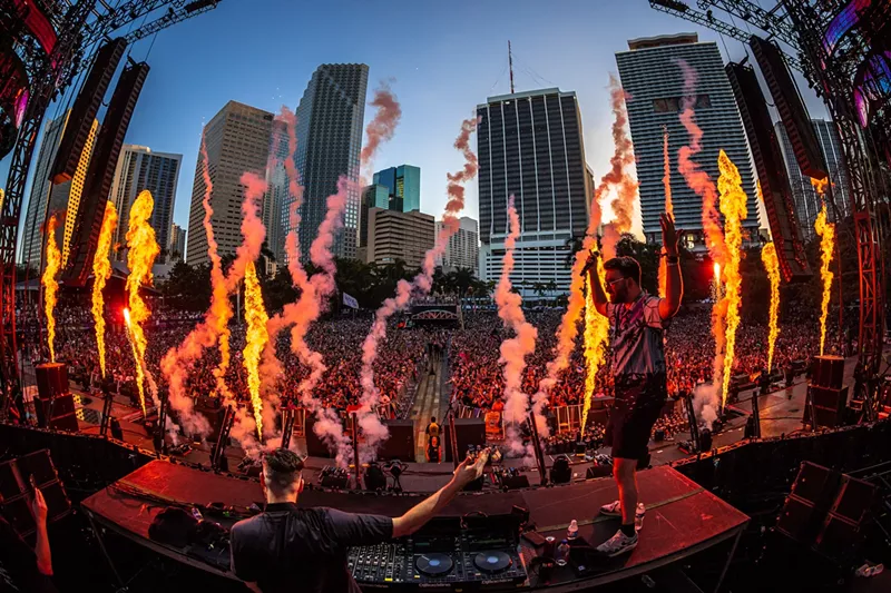 Image: DJ performing on the main stage at Ultra in front of a huge crowd against the downtown Miami skyline